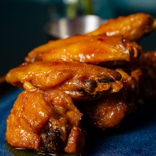Pile of glossy, golden-brown chicken wings with chili flakes on a dark blue plate.