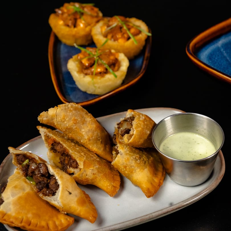 Golden empanadas with savory meat filling and green sauce, plus garnished mini tarts.