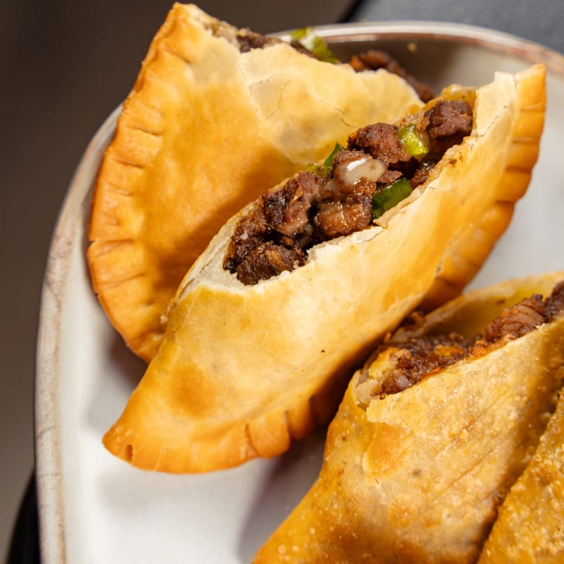 Golden-fried empanadas with a savory meat and vegetable filling, served on a white plate.