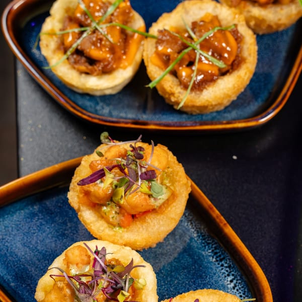 Crispy mini tartlets filled with savory shrimp and glazed meat, garnished with fresh herbs.