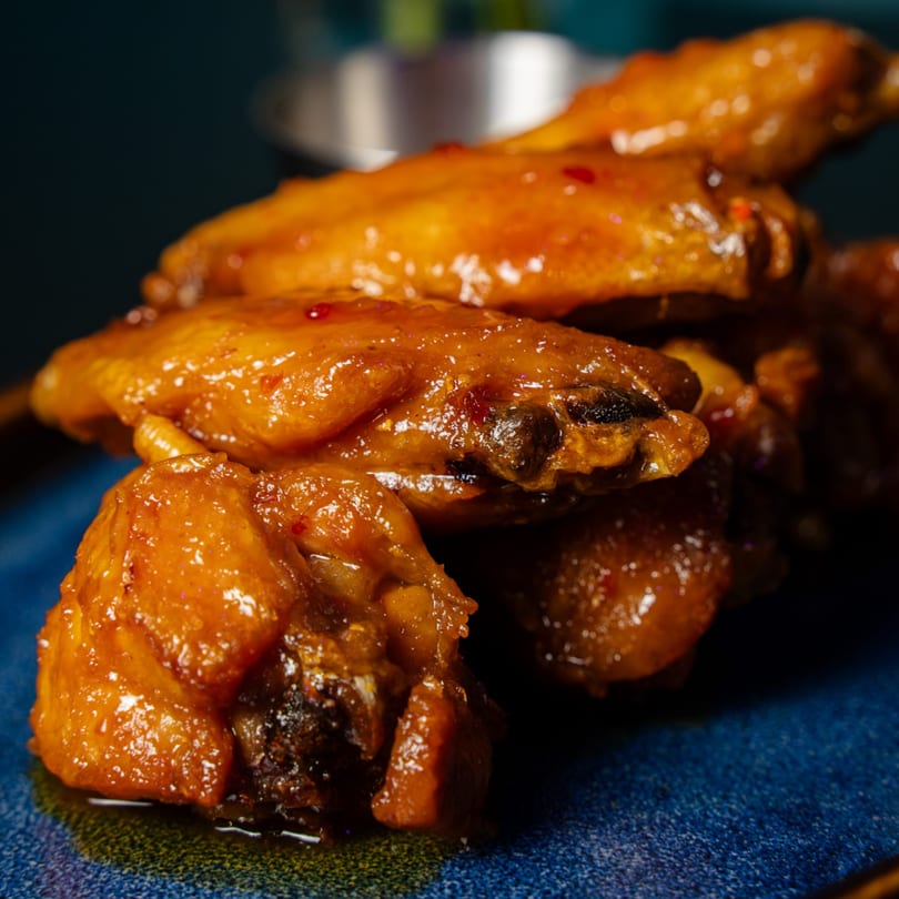 Pile of golden-brown glazed chicken wings with red flakes on a blue plate.