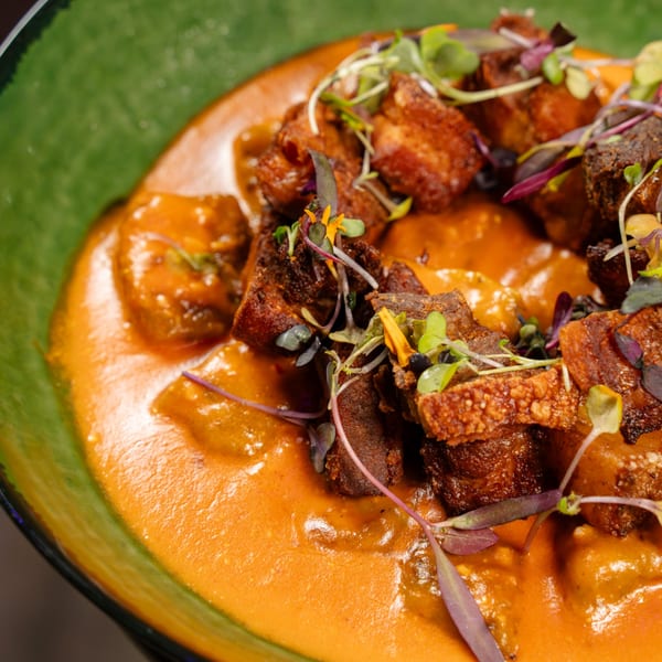 Crispy pork belly in a creamy orange sauce, topped with microgreens and edible flowers.