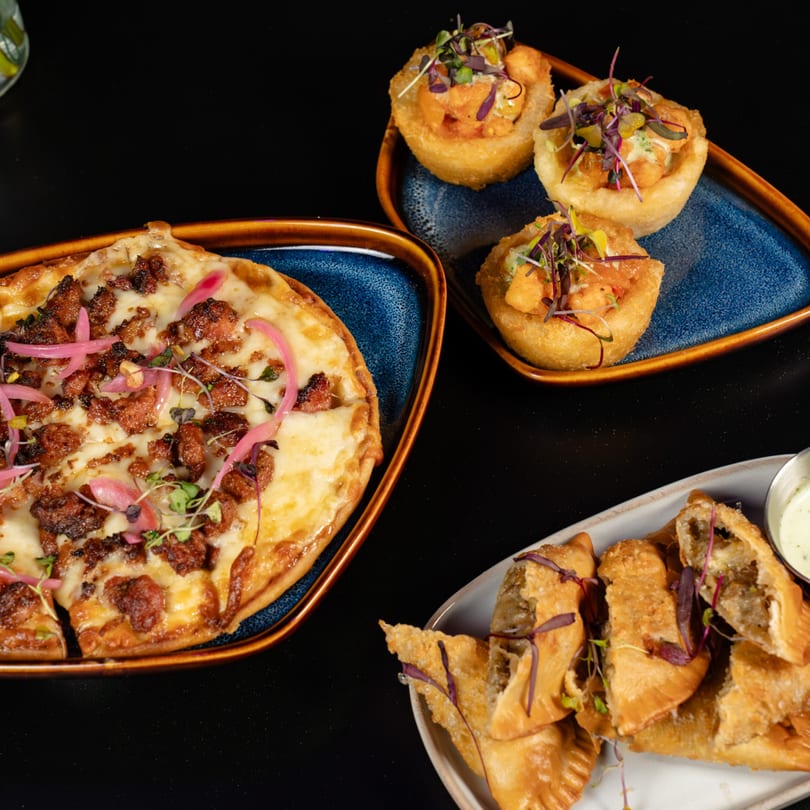 Flatbread pizza with meat and red onions, fried appetizer cups, and empanadas with dipping sauce.