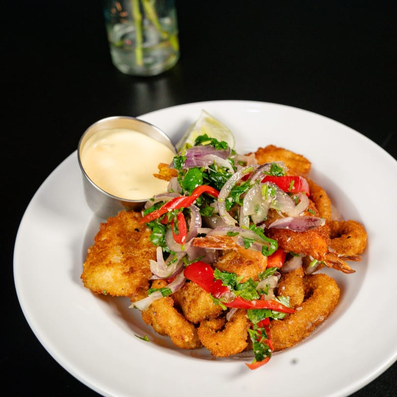 Crispy fried seafood with a vibrant red onion and cilantro topping, served with a creamy dipping sauce.