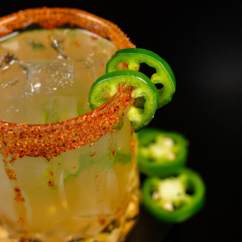 Spicy cocktail with a chili-rimmed glass, ice, and jalapeño slices.