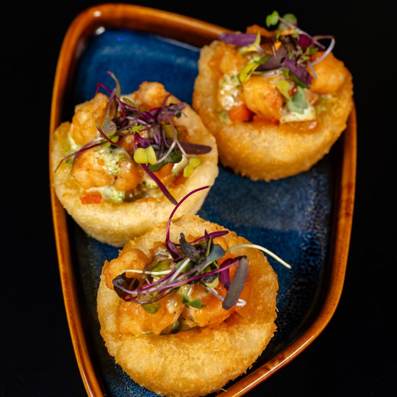 Three fried pastry cups filled with shrimp, sauce, and microgreens on a blue plate.