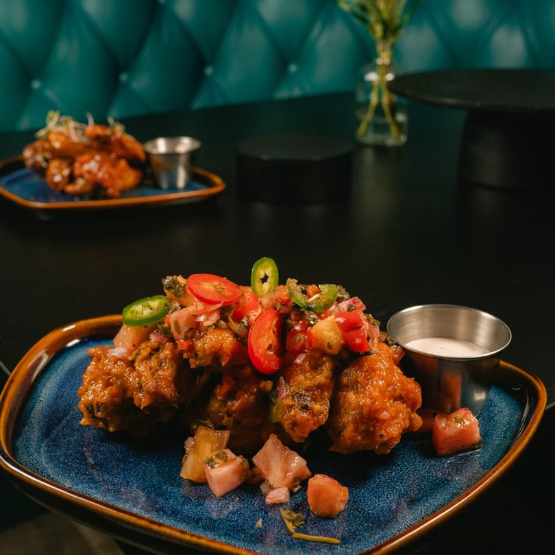 Glazed chicken wings with fresh salsa and jalapeños, served with dipping sauce on a blue plate.